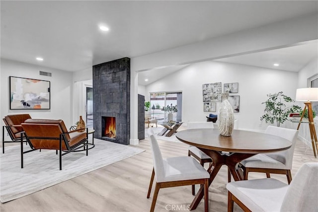 dining space featuring a tile fireplace, light hardwood / wood-style flooring, and lofted ceiling