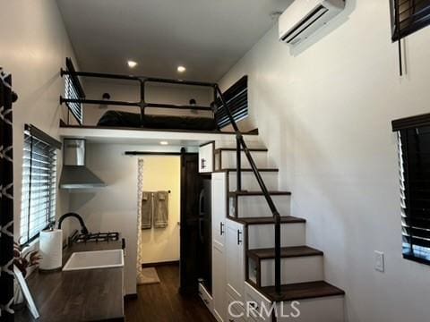 kitchen with wall chimney range hood, sink, dark hardwood / wood-style floors, a barn door, and a wall unit AC