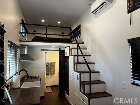 kitchen with wall chimney range hood, sink, an AC wall unit, a barn door, and dark hardwood / wood-style flooring