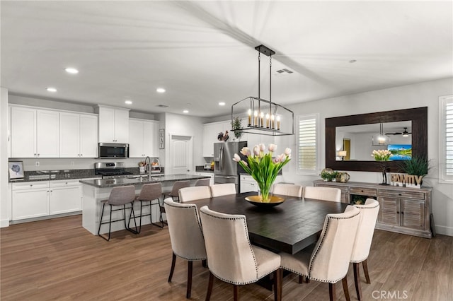 dining space with ceiling fan with notable chandelier, sink, and dark wood-type flooring