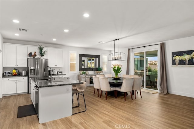 kitchen featuring white cabinetry, an island with sink, light hardwood / wood-style floors, and decorative light fixtures