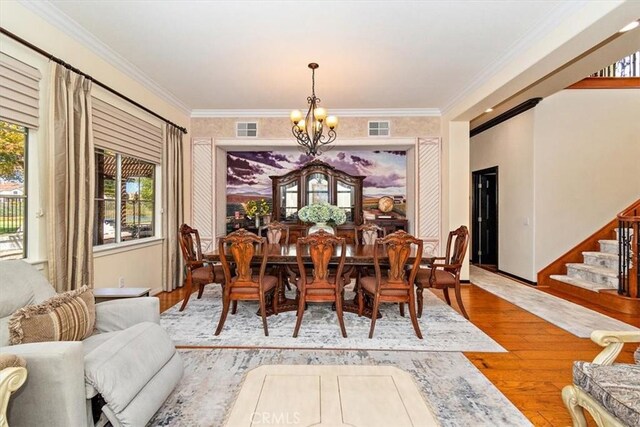 dining space with hardwood / wood-style flooring, ornamental molding, and an inviting chandelier