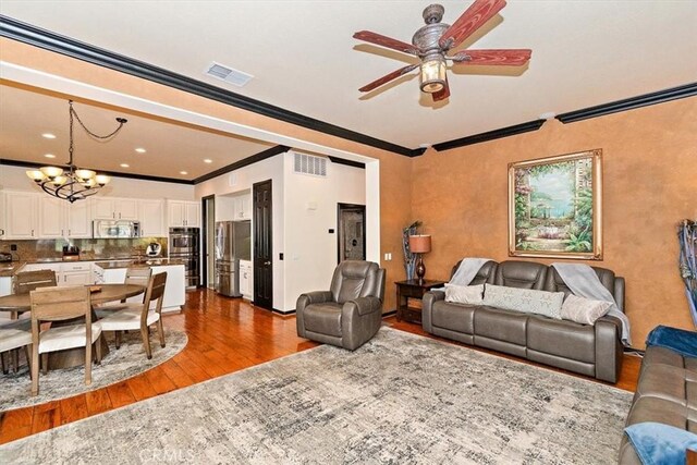 living room with ceiling fan with notable chandelier, wood-type flooring, and ornamental molding