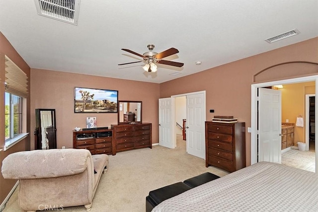 bedroom with ceiling fan, light colored carpet, and ensuite bath