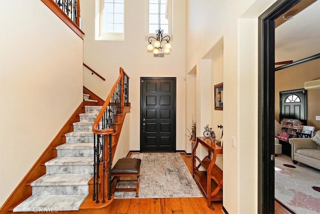 foyer entrance featuring light hardwood / wood-style floors, a towering ceiling, and a chandelier