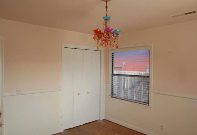 unfurnished bedroom with wood-type flooring, a notable chandelier, and a closet