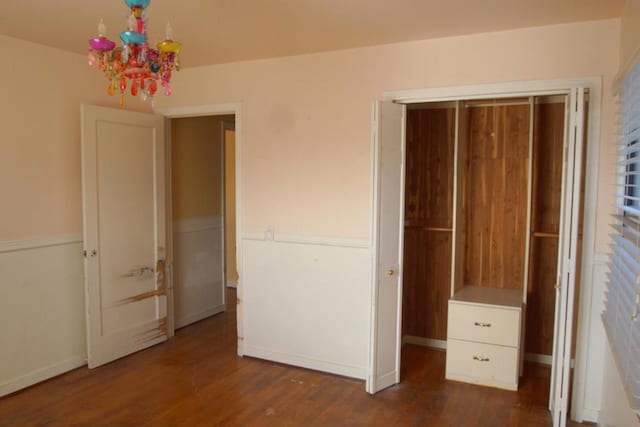 unfurnished bedroom with a closet, dark hardwood / wood-style flooring, and an inviting chandelier