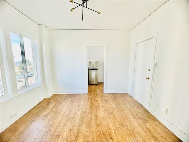 unfurnished room with a chandelier and light wood-type flooring