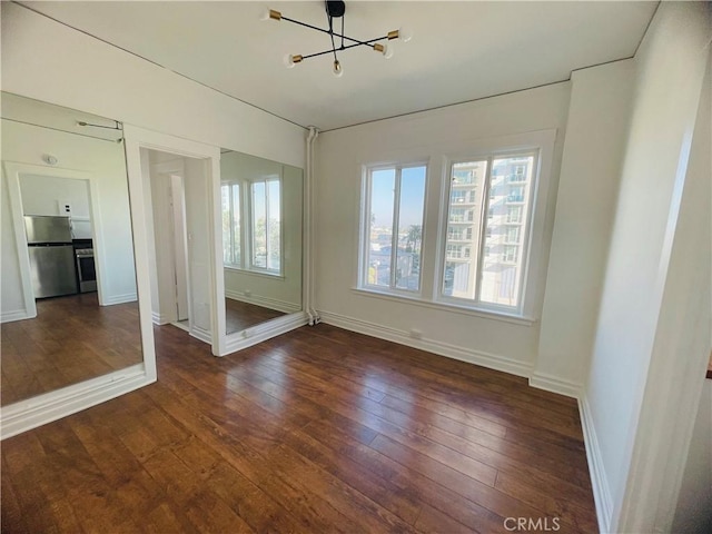 unfurnished room with a notable chandelier and dark wood-type flooring