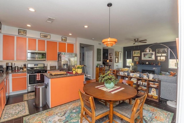 kitchen with dark wood-type flooring, dark stone countertops, a kitchen island, ceiling fan, and stainless steel appliances