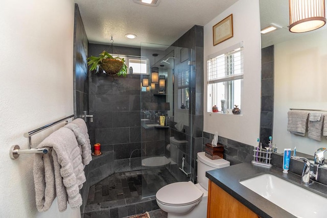 bathroom with vanity, toilet, a healthy amount of sunlight, and tiled shower