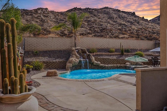 pool at dusk with a mountain view, pool water feature, and a patio area