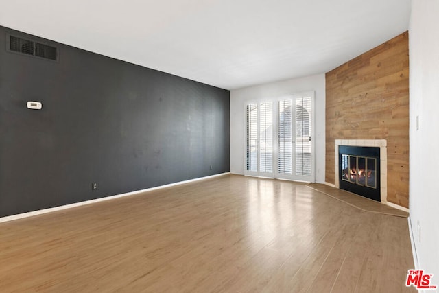 unfurnished living room with light hardwood / wood-style floors, wood walls, and a tiled fireplace