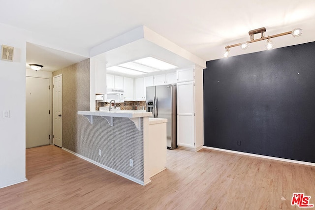 kitchen featuring white cabinets, a kitchen breakfast bar, kitchen peninsula, light wood-type flooring, and stainless steel fridge with ice dispenser