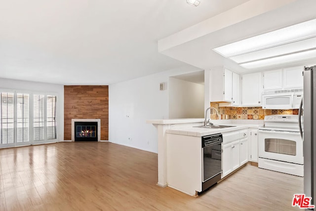 kitchen with kitchen peninsula, light wood-type flooring, white appliances, sink, and a fireplace