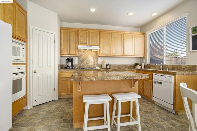 kitchen featuring sink, white appliances, a breakfast bar, a center island, and decorative backsplash