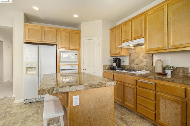 kitchen featuring a breakfast bar, a center island, white appliances, and decorative backsplash