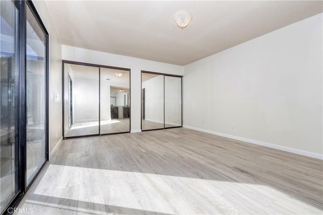 unfurnished bedroom featuring light hardwood / wood-style flooring and two closets