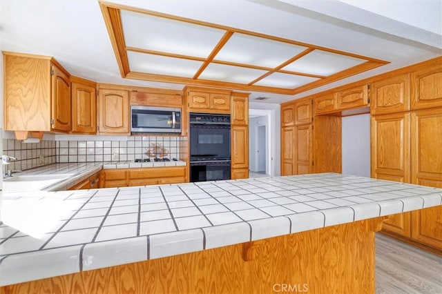 kitchen featuring backsplash, black double oven, tile counters, light hardwood / wood-style floors, and kitchen peninsula