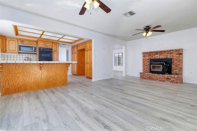 kitchen with a kitchen breakfast bar, a wood stove, tile countertops, light hardwood / wood-style flooring, and black oven