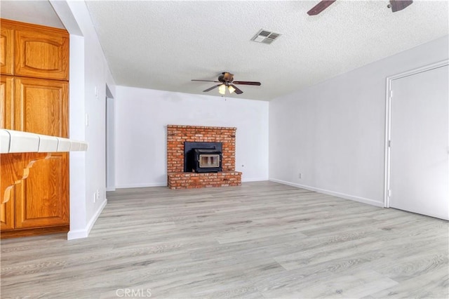 unfurnished living room featuring a wood stove, ceiling fan, a textured ceiling, and light wood-type flooring