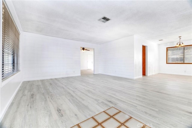 empty room with ceiling fan with notable chandelier and light hardwood / wood-style floors