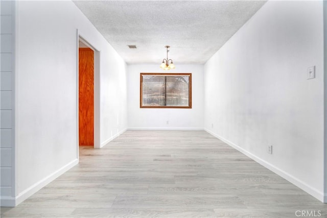 empty room featuring a chandelier, a textured ceiling, and light wood-type flooring