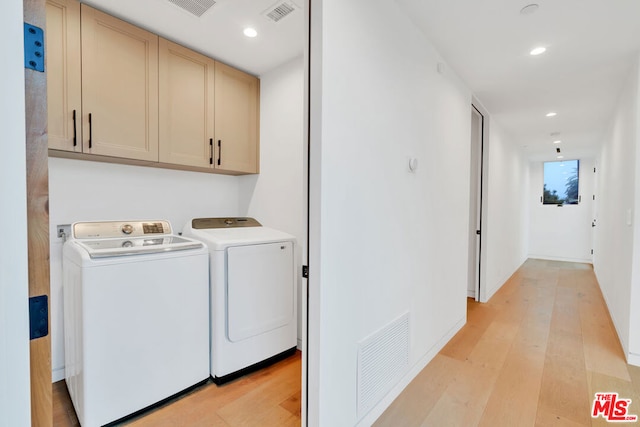 clothes washing area featuring light hardwood / wood-style flooring, cabinets, and independent washer and dryer