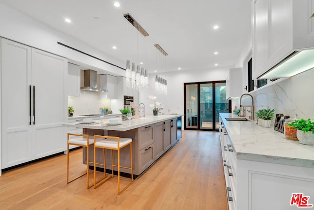 kitchen featuring wall chimney exhaust hood, sink, white cabinets, hanging light fixtures, and a large island