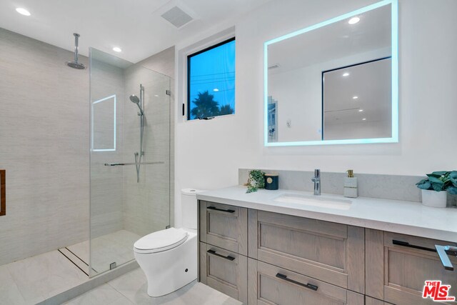 bathroom with tiled shower, vanity, toilet, and tile patterned flooring