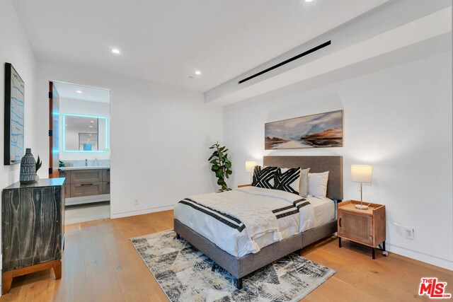 bedroom with a barn door, light wood-type flooring, and connected bathroom