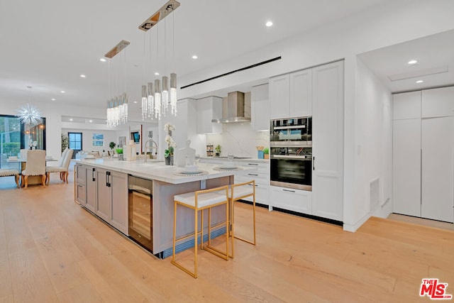 kitchen with white cabinets, pendant lighting, wall chimney exhaust hood, and a spacious island