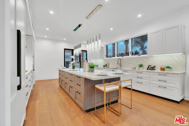 kitchen with white cabinetry, hanging light fixtures, a spacious island, and light hardwood / wood-style floors