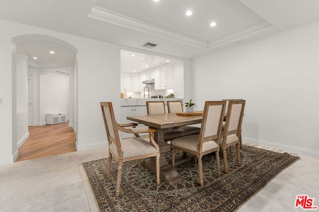 carpeted dining area with sink, a tray ceiling, and ornamental molding