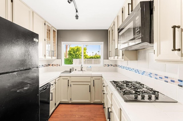 kitchen featuring sink, backsplash, light hardwood / wood-style flooring, and black appliances