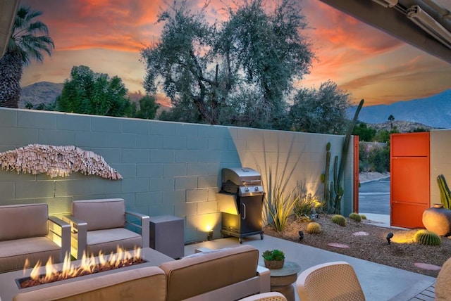 patio terrace at dusk featuring a mountain view, a grill, and an outdoor living space with a fire pit