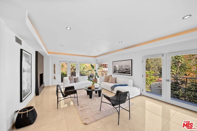 tiled living room with a healthy amount of sunlight, a raised ceiling, and french doors