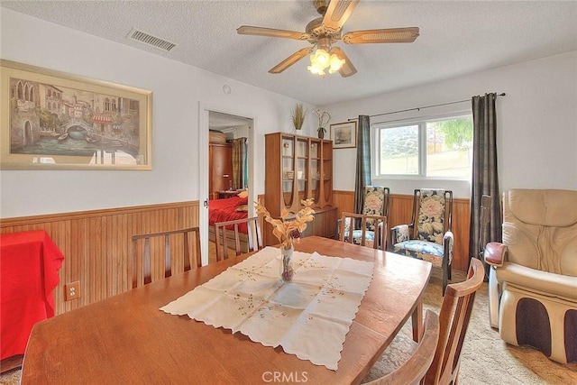 dining space with ceiling fan, wood walls, light colored carpet, and a textured ceiling