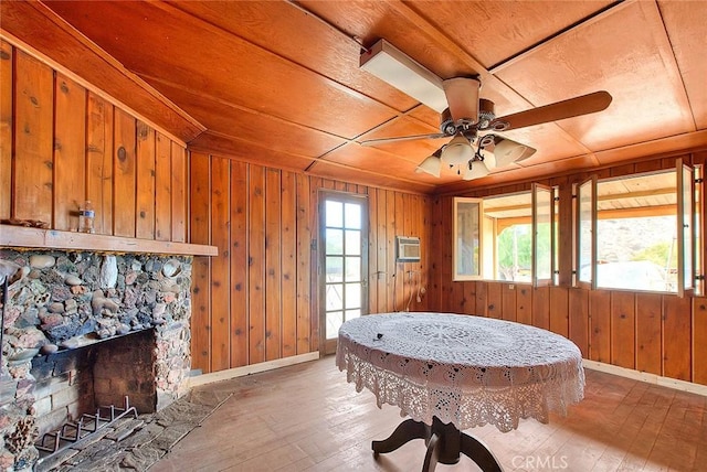 interior space with hardwood / wood-style flooring, ceiling fan, wood walls, and a stone fireplace