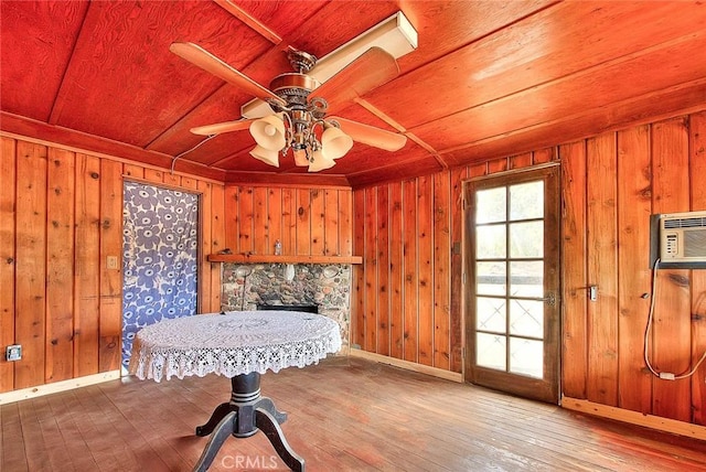 interior space featuring a wall mounted air conditioner, ceiling fan, wooden walls, a fireplace, and hardwood / wood-style floors