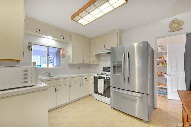 kitchen with white gas stove, cream cabinetry, stainless steel refrigerator with ice dispenser, and sink