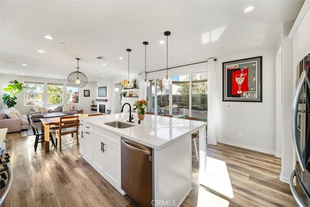 kitchen featuring stainless steel appliances, a kitchen island with sink, pendant lighting, white cabinets, and sink