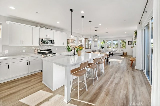 kitchen featuring white cabinetry, stainless steel appliances, an island with sink, a kitchen breakfast bar, and sink