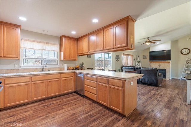 kitchen featuring kitchen peninsula, ceiling fan, dark wood-type flooring, sink, and a tile fireplace