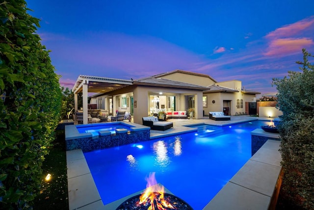 pool at dusk featuring pool water feature, an in ground hot tub, an outdoor living space with a fire pit, area for grilling, and a patio