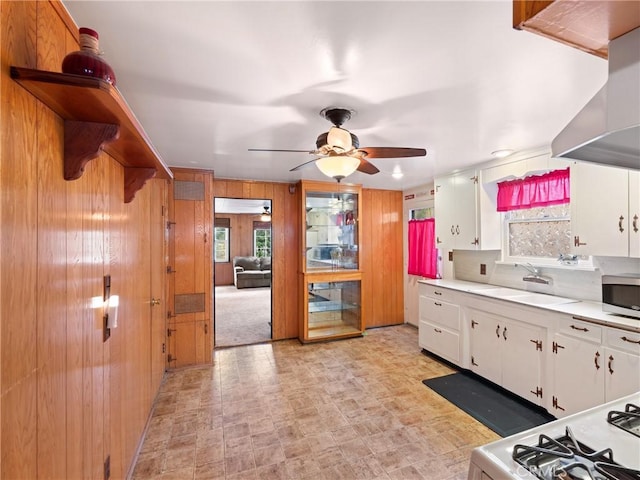 kitchen featuring white cabinetry, wall chimney exhaust hood, wood walls, and sink