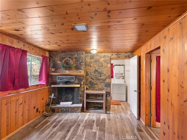 unfurnished living room with a stone fireplace, wooden walls, washer / dryer, wood-type flooring, and wood ceiling