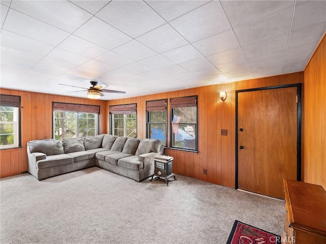 carpeted living room featuring wooden walls and ceiling fan