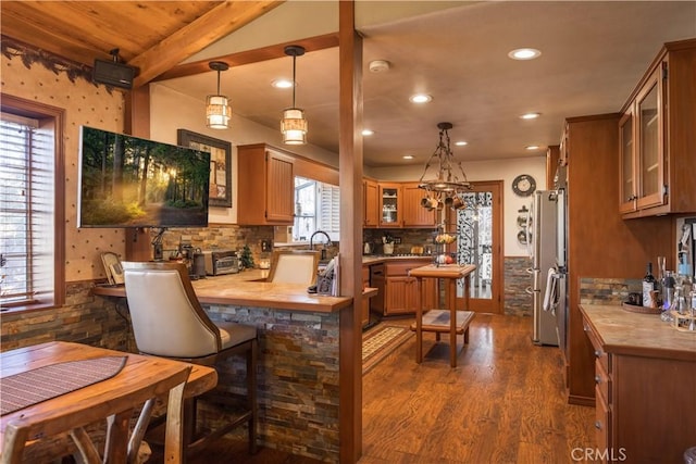 kitchen with pendant lighting, dark wood-type flooring, stainless steel fridge, backsplash, and kitchen peninsula