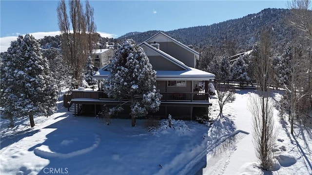 snow covered back of property with a mountain view and covered porch